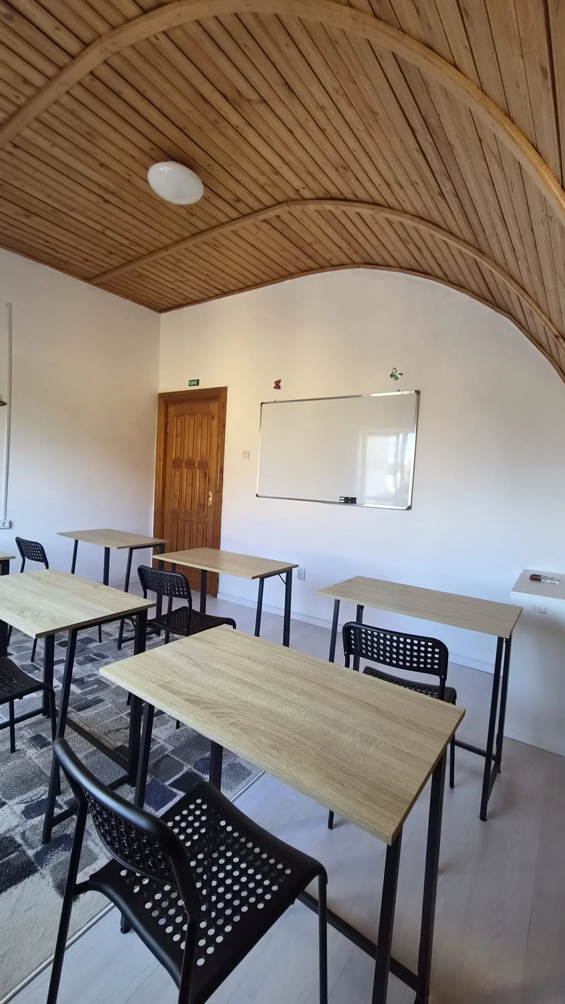 Sala cu tavan de lemn arcuit, tablă albă și mese individuale